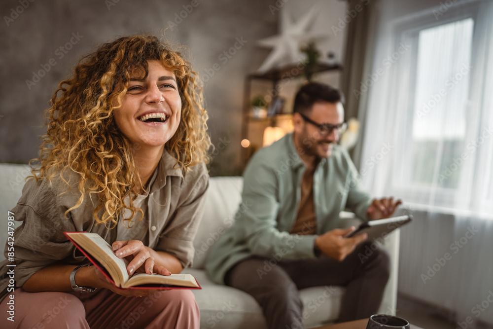 Girlfriend read a book while his boyfriend use tablet at home Girlfriend read a book while his boyfriend use tablet at home