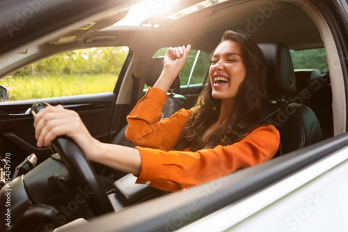 Konstfotografi Overjoyed pretty young woman driver listening to music and singing while holding