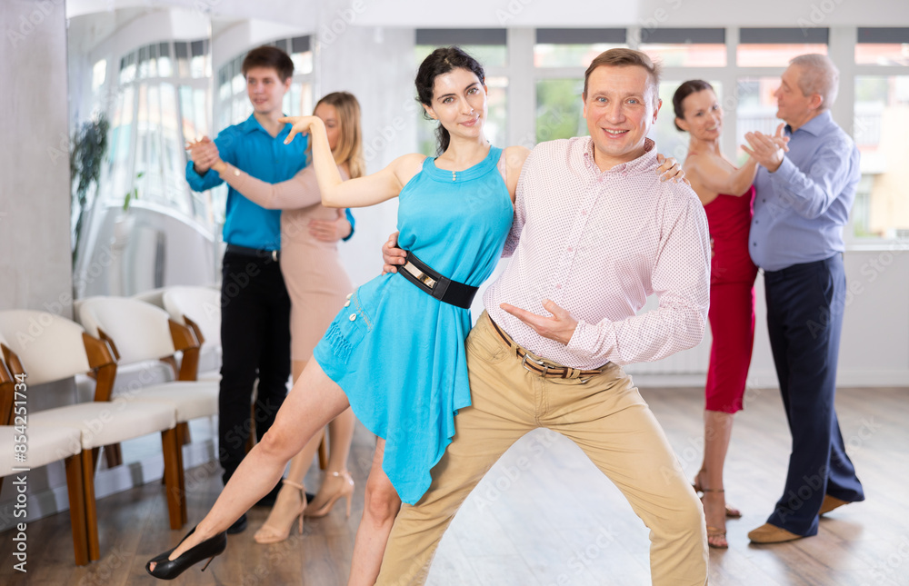 Fototapeta premium Happy couple of amateur dancers practicing elegant slow foxtrot, skillfully performing support in dance studio ..