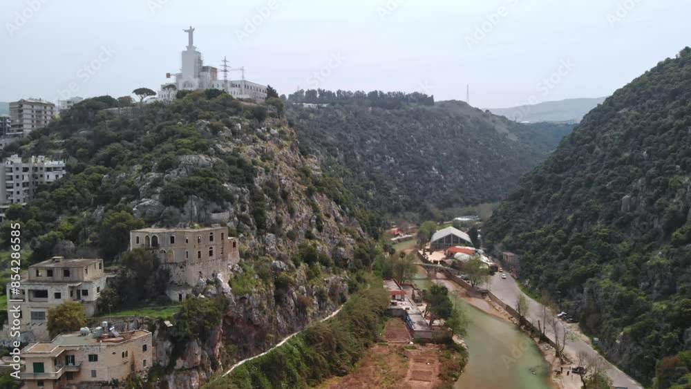 Statue of Jesus on a hilltop in Lebanon overlooking a valley with buildings and greenery at the mouth of Nahr El Kalb, Lycus River Statue of Jesus on a hilltop in Lebanon overlooking a valley with buildings and greenery at the mouth of Nahr El Kalb, Lycus River