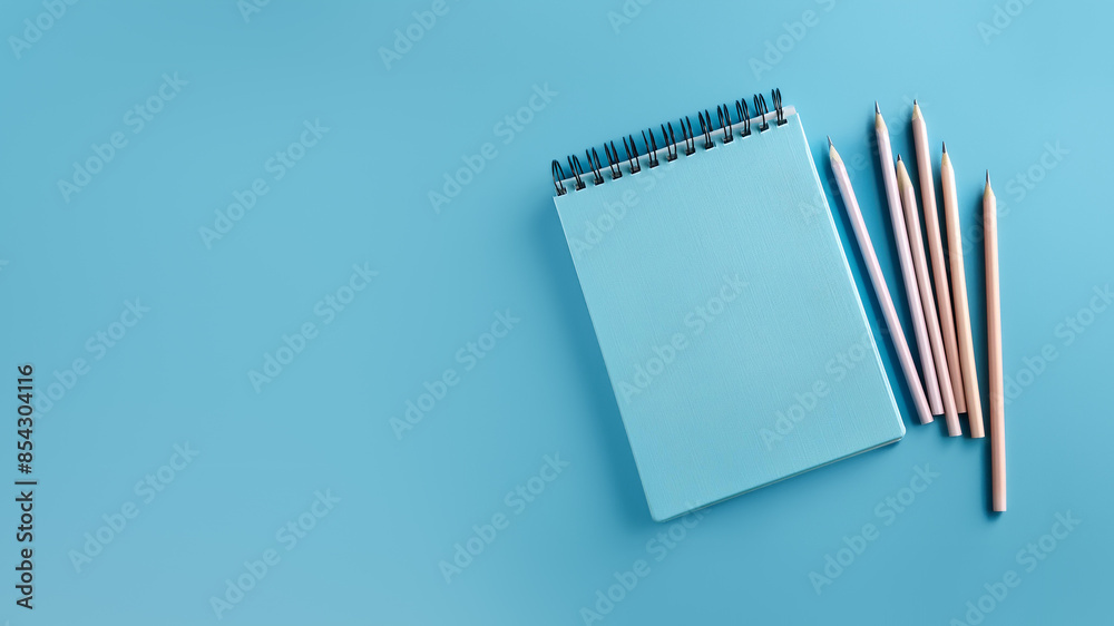Blue spiral notebook with wooden pencils on a light blue background. Top view. Study or workspace mockup with copy space. Blue spiral notebook with wooden pencils on a light blue background. Top view. Study or workspace mockup with copy space.