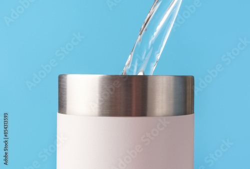 Water pours into thermal mug or thermos on blue background.