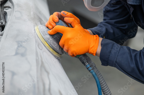 A mechanic sands the putty on a car body with a machine. Repair after an accident.  photo