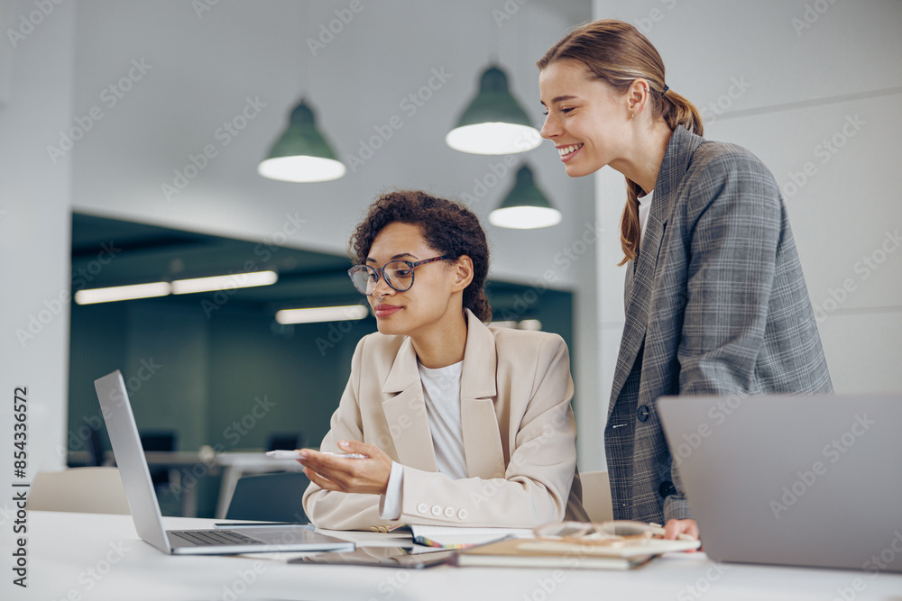 Two busy female coworkers discussing project while working in office and use laptop Two busy female coworkers discussing project while working in office and use laptop