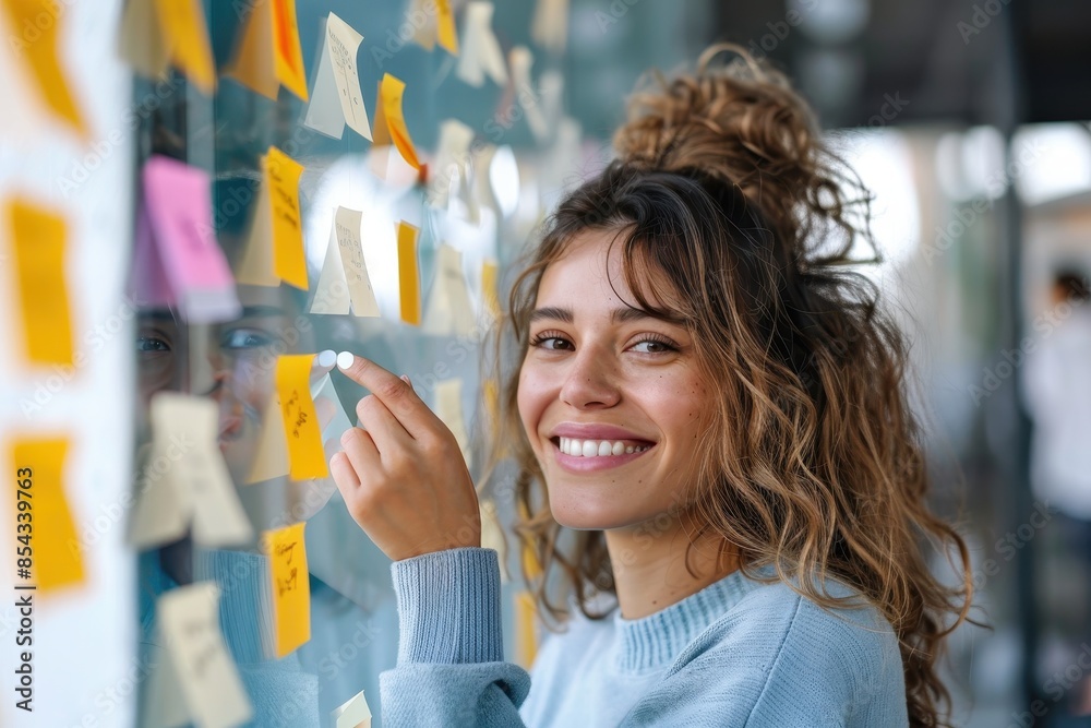 An animated and creative young woman sticks notes on a glass partition in a modern office, representing brainstorming and innovation An animated and creative young woman sticks notes on a glass partition in a modern office, representing brainstorming and innovation