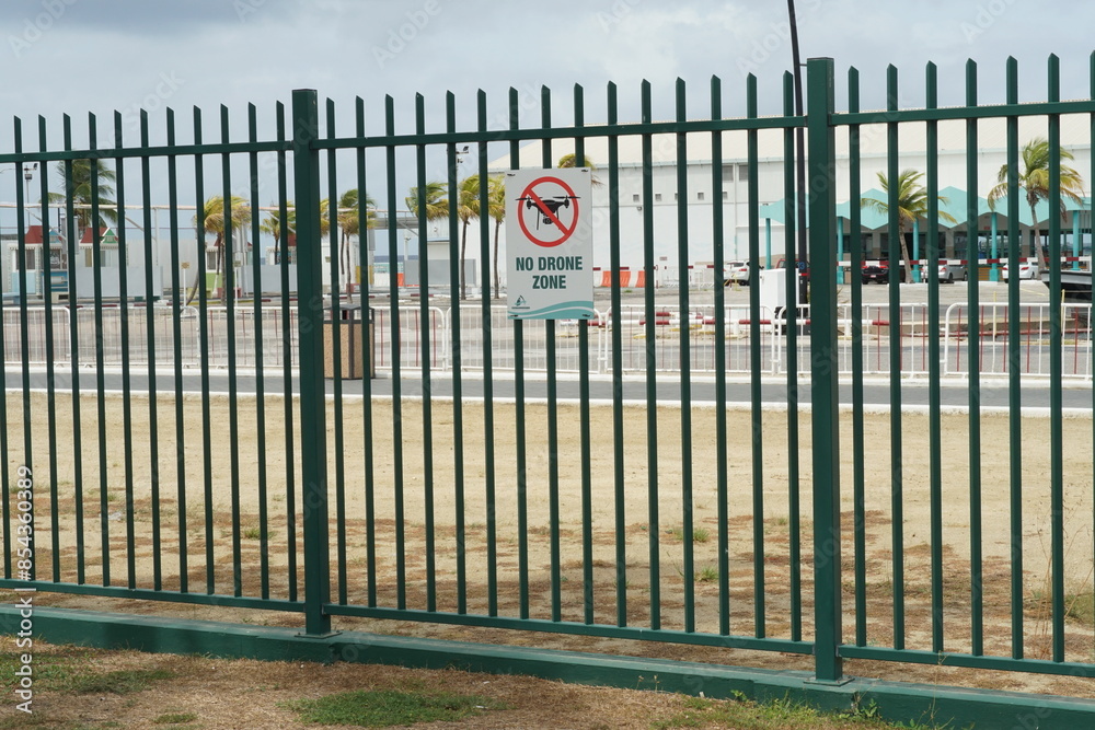 Oranjestad, Aruba, May 24, 2024: Sign with silhouette of drone in crossed red circle and text no drone zone situated on green fence separating of port facilities in Oranjestad, Aruba. 