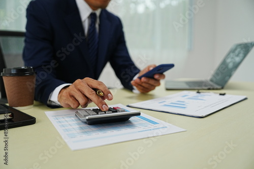 professional businessman is sitting in his office, confidently smiling while working on his laptop. A successful entrepreneur and leader, he embodies corporate success and happiness