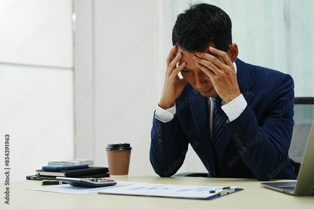 stressed businessman is sitting at his office desk, looking worried while working on his laptop. Overworked and frustrated, he faces financial problems and job pressures in his corporate banking role stressed businessman is sitting at his office desk, looking worried while working on his laptop. Overworked and frustrated, he faces financial problems and job pressures in his corporate banking role