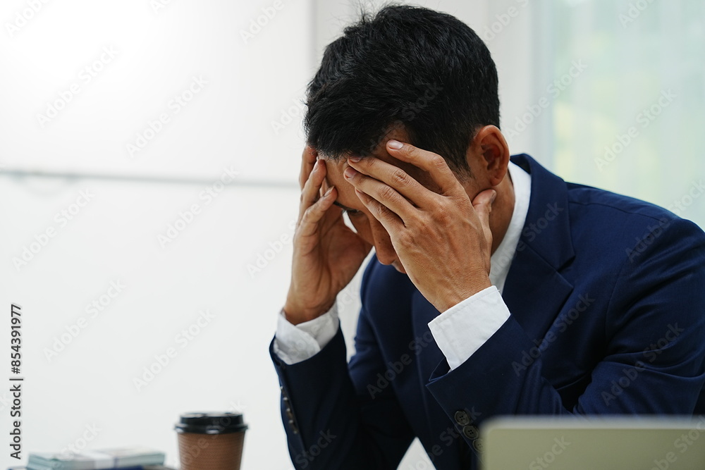 stressed businessman is sitting at his office desk, looking worried while working on his laptop. Overworked and frustrated, he faces financial problems and job pressures in his corporate banking role stressed businessman is sitting at his office desk, looking worried while working on his laptop. Overworked and frustrated, he faces financial problems and job pressures in his corporate banking role