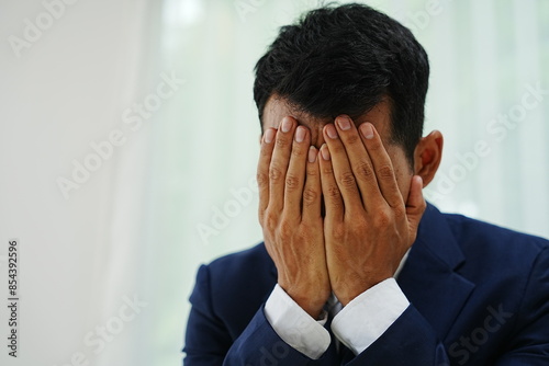 stressed businessman is sitting at his office desk, looking worried while working on his laptop. Overworked and frustrated, he faces financial problems and job pressures in his corporate banking role