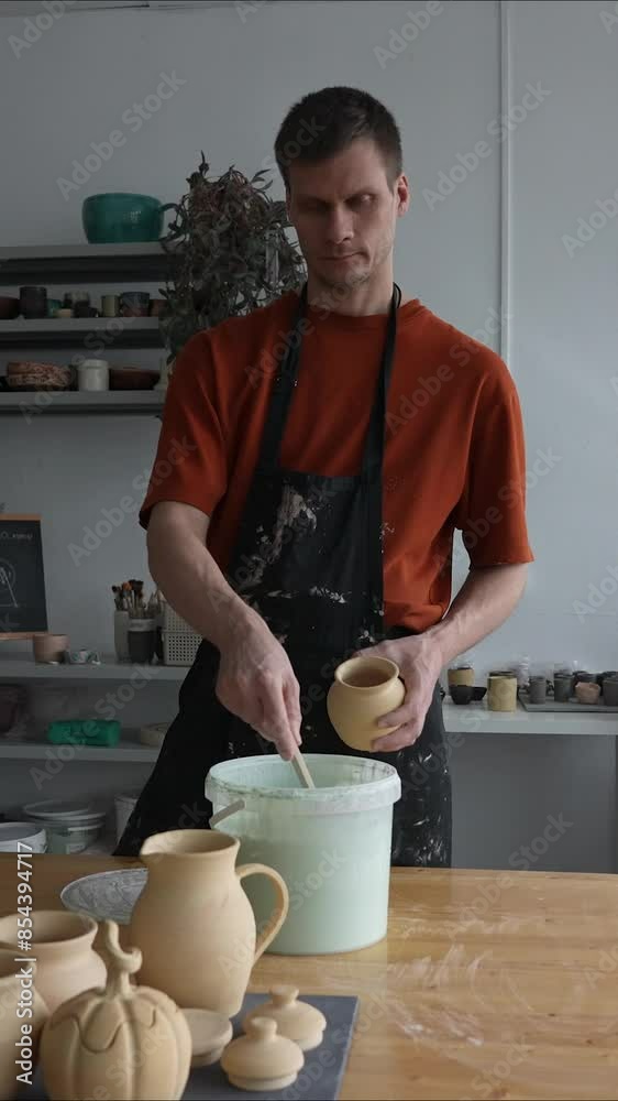 A potter applies glaze to a ceramic pot with a brush. Vertical video. A potter applies glaze to a ceramic pot with a brush. Vertical video.