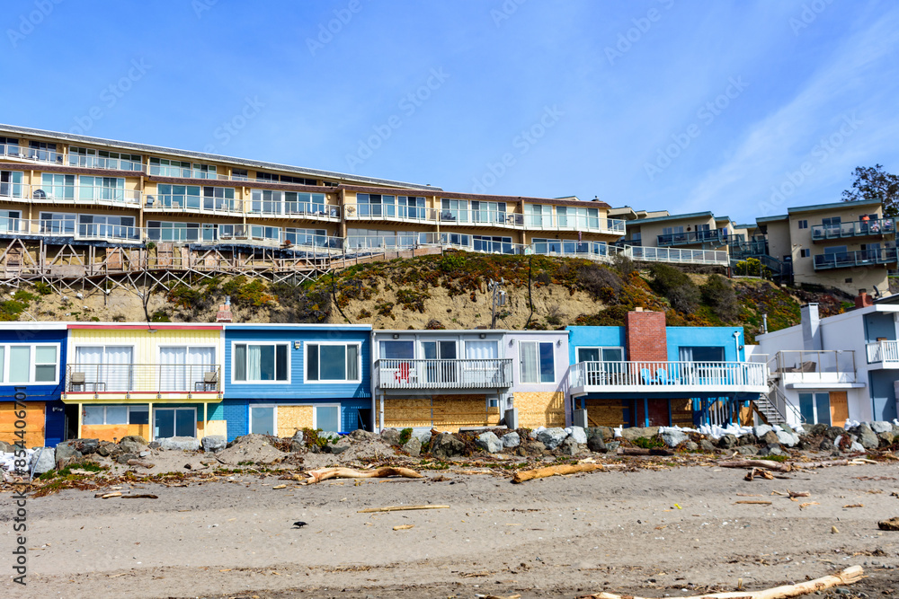 Obraz premium Beachfront houses overlook a sandy Rio Del Mar Beach strewn with debris. The front row of coastal home boarded up with plywood to prevent or reduce flood water damage