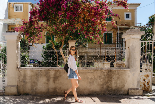 A young woman enjoys a leisurely walk by a vibrant bougainvillea in full bloom on a sunny day, showcasing the beauty of springtime.