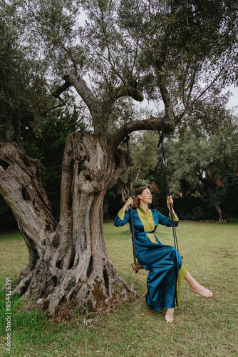 A carefree woman swings under a majestic olive tree in a serene garden, embodying freedom and leisure in nature.