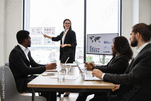 Wallpaper Mural Business woman giving presentation to multiracial colleagues standing near graphs and charts on panoramic window. Team includes people working with laptops, discussing strategy, analyzing data. Torontodigital.ca