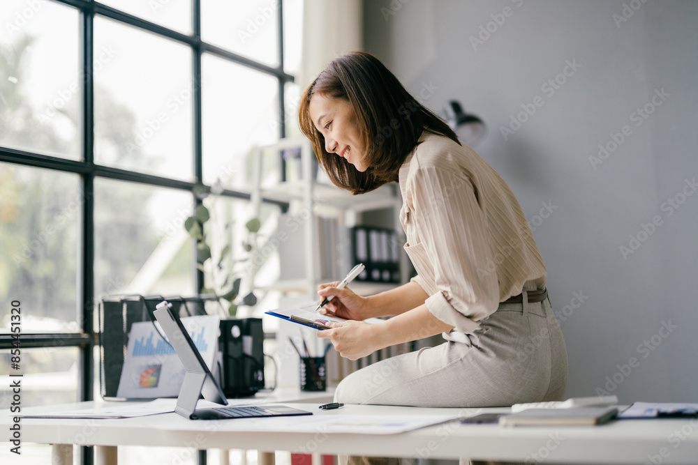Young Professional Woman Working on Tablet in Modern Office with Large Windows and Natural Light Young Professional Woman Working on Tablet in Modern Office with Large Windows and Natural Light