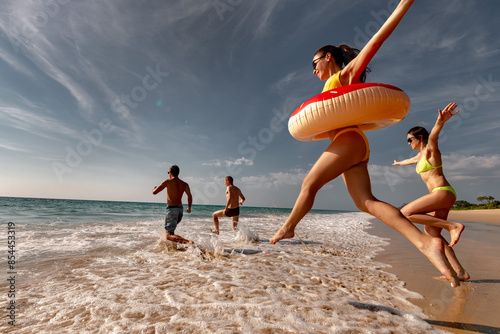 Canvas Print Happy friends runs and jumps with inflatable donuts to sea beach