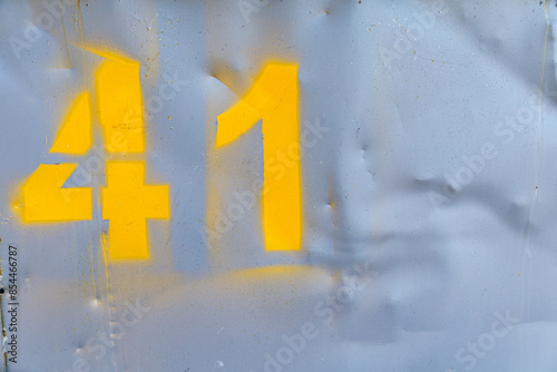 Metal sheet painted with gray color with yellow spray painted number 41. Empty deformed metal wall texture background. Distorted grunge gray metal sheet with number. 