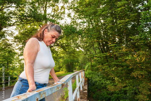 Eine Frau im Alter über 60 steht am Geländer einer Brücke photo