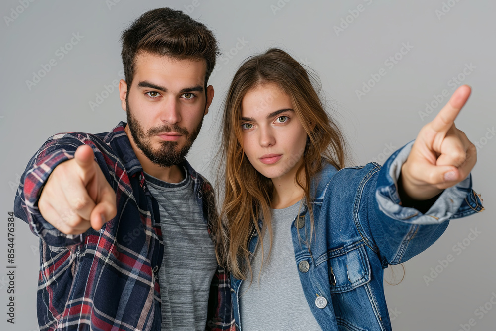Naklejka premium Young couple or friends, a man and woman in casual clothing, pointing directly at the camera with engaging expressions