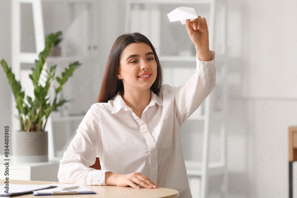 Young businesswoman with paper plane sitting at table in office Young businesswoman with paper plane sitting at table in office