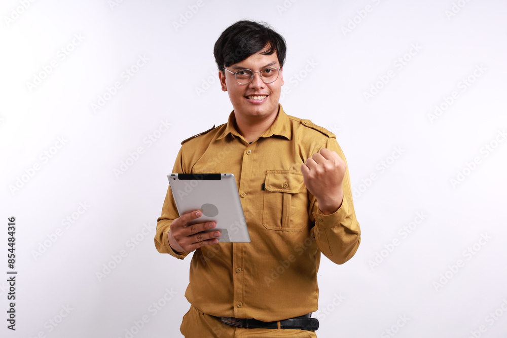 a young handsome Indonesian civil servant isolated over white background feeling excited while holding tablet pc a young handsome Indonesian civil servant isolated over white background feeling excited while holding tablet pc