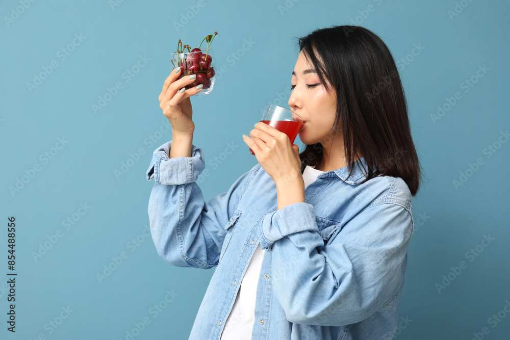 Beautiful Asian woman with cherries drinking juice on blue background Beautiful Asian woman with cherries drinking juice on blue background