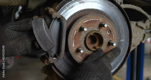 Auto mechanic showing uneven brake pad wear on an old brake disc, work process of inspecting car parts at a technical inspection station