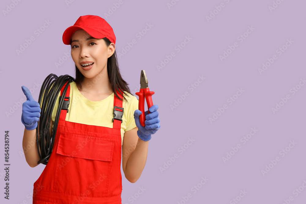 Young female electrician with cables and pliers showing thumb-up on purple background Young female electrician with cables and pliers showing thumb-up on purple background