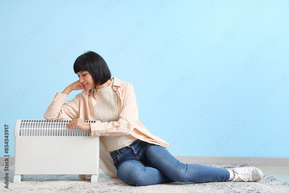 Young woman with radiator sitting near blue wall Young woman with radiator sitting near blue wall