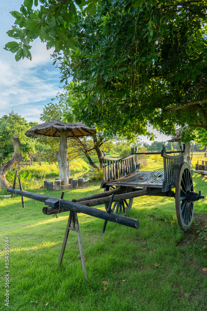 A wooden cart used for carrying goods, which was placed on the backs of oxen in the past, is placed under a tree near a roadside rest area, looking naturally beautiful. A wooden cart used for carrying goods, which was placed on the backs of oxen in the past, is placed under a tree near a roadside rest area, looking naturally beautiful.