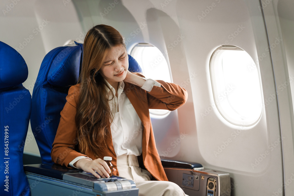 Fototapeta premium A young Asian woman is sitting in her seat as an airplane passenger, experiencing airsickness with symptoms like nausea, vomiting, dizziness, and general discomfort.