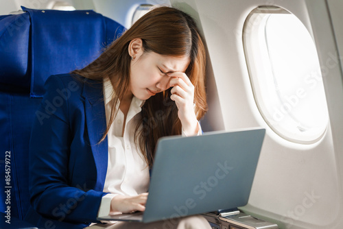 A young Asian woman is sitting in her seat as an airplane passenger, experiencing airsickness with symptoms like nausea, vomiting, dizziness, and general discomfort. photo