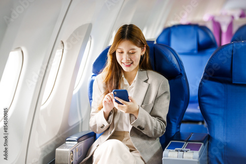 A young Asian woman, seated as an airplane passenger, uses Wi-Fi for shopping, emailing, and placing online orders, enhancing her travel experience with connectivity.