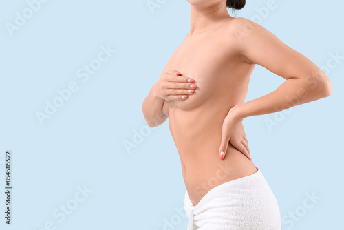 Naked young woman covering her breasts on blue background, closeup photo