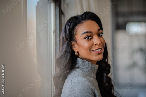Close-up portrait of a young african-american woman standing at the window and looking at camera
