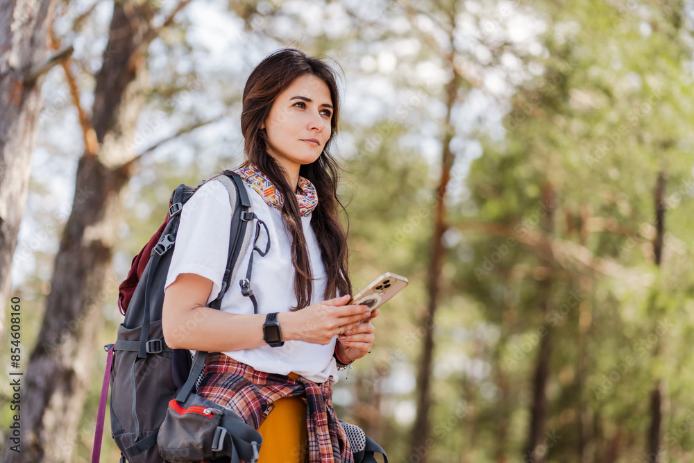 Young woman holding smartphone and checking gps while relaxing in the forest after hiking Young woman holding smartphone and checking gps while relaxing in the forest after hiking