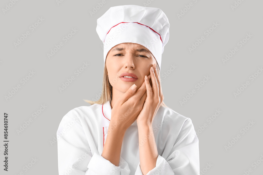 Young female chef suffering from tooth ache on grey background Young female chef suffering from tooth ache on grey background