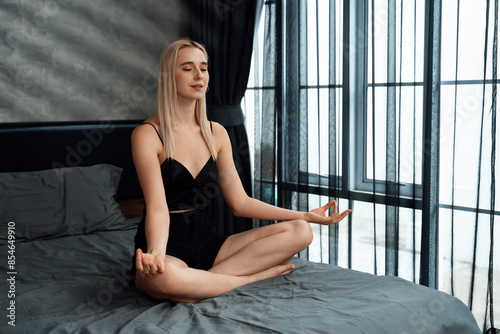 Young woman doing morning yoga and meditation in her bedroom, enjoying the solitude and practicing meditative poses. Mindfulness activity and healthy mind lifestyle. Blithe