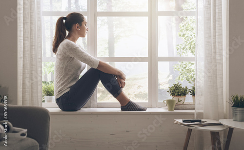 Fotografía Woman sitting next to a window and looking away