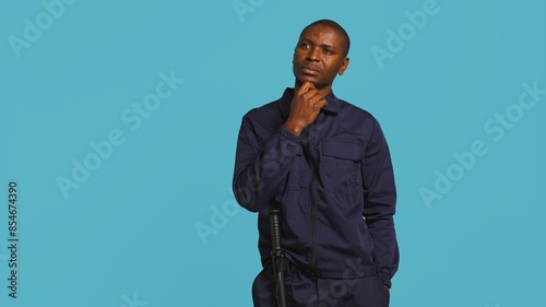 Security guard doing thinking hand gesture, being tasked with preventing criminal activity and detaining suspects. Portrait of pensive bodyguard rubbing chin, studio background, camera B