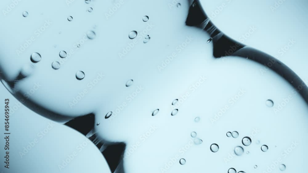 Macro shot of drops of pure fresh melt mountain water with tiny air bubbles, the drops are moving and merging into a large water sphere on a bright light blue background