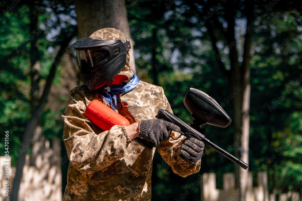 Fototapeta premium in the wild near tree structures player in a pintball uniform holds a pistol with a red balloon team game camouflage clothing