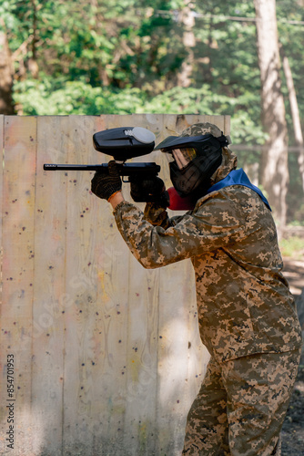 Konstfotografi in the wild near tree structures player in a pintball uniform holds a pistol wit