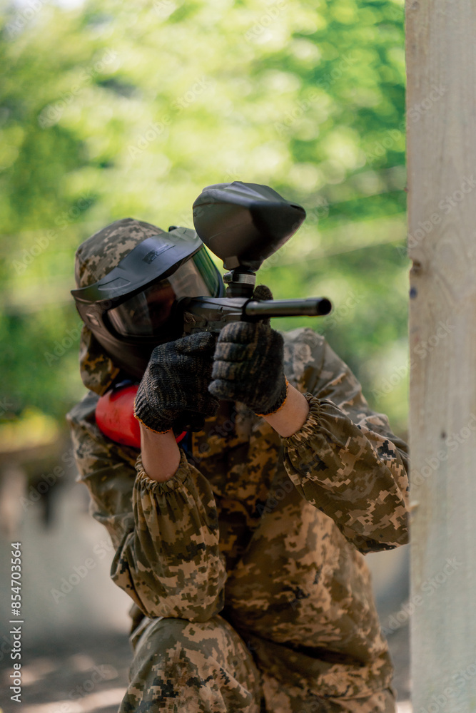 Fototapeta premium close up in the wild near tree structures player in a pintball uniform holds a pistol with a red balloon team game camouflage clothing