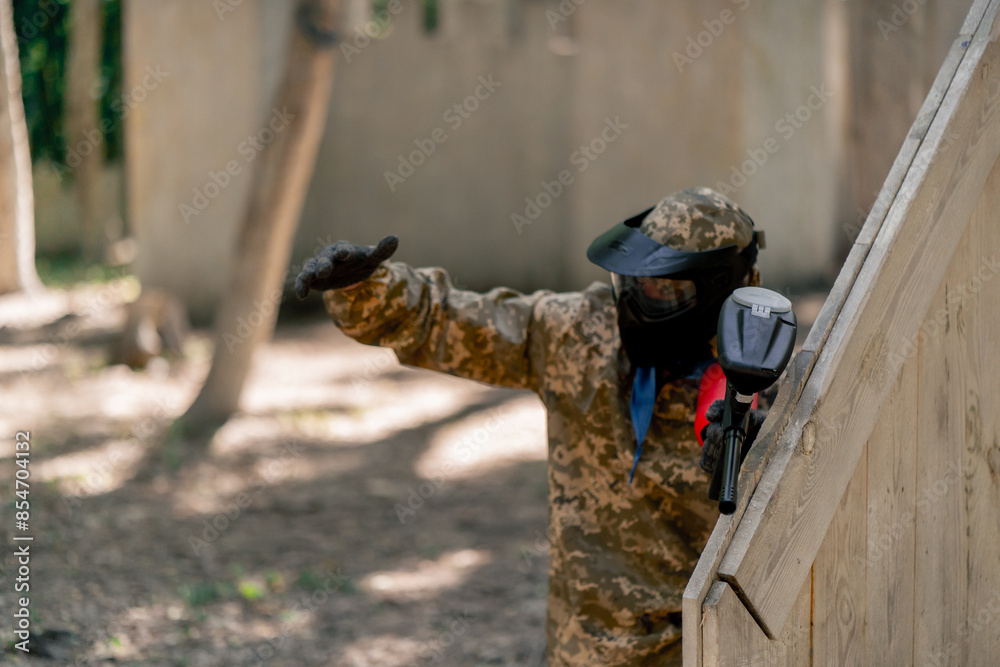 Obraz premium in the wild near tree structures player in a pintball uniform holds a pistol with a balloon team game camouflage clothing communication using hands