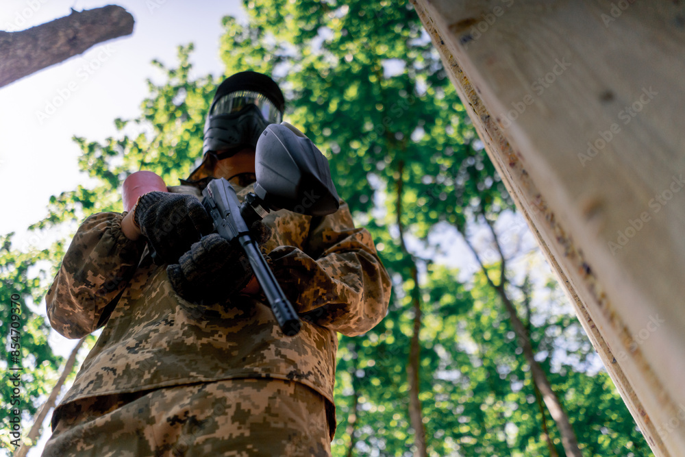Fototapeta premium low shot in the wild near tree structures player in a pintball uniform holds a pistol with a red balloon team game camouflage clothing