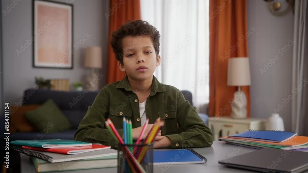 Serious tired sad calm African American ethnic little boy child kid son at home apartment distant education studying at table looking at camera look posing learning study homework childcare health