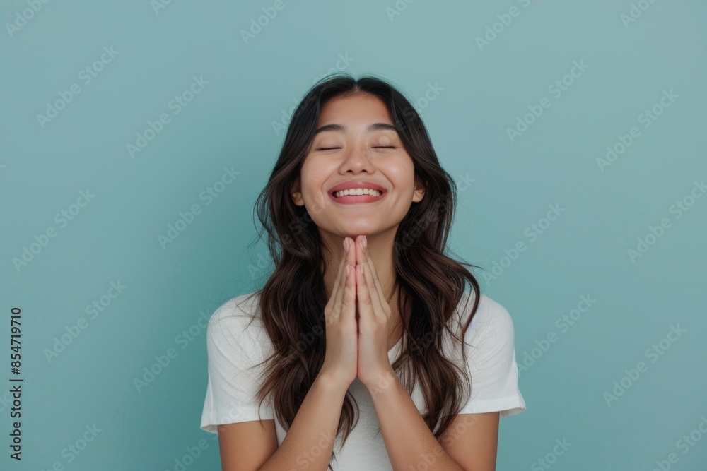 Portrait of a happy asian woman in her 20s joining palms in a gesture of gratitude on soft blue background Portrait of a happy asian woman in her 20s joining palms in a gesture of gratitude on soft blue background