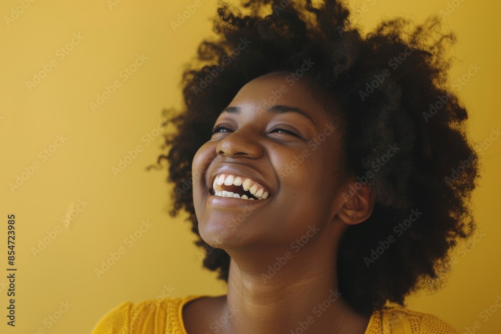 Portrait of a tender afro-american woman in her 20s laughing while standing against soft yellow background Portrait of a tender afro-american woman in her 20s laughing while standing against soft yellow background